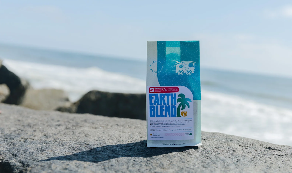 Earth Blend coffee bag on a rocky beach with the ocean in the background.