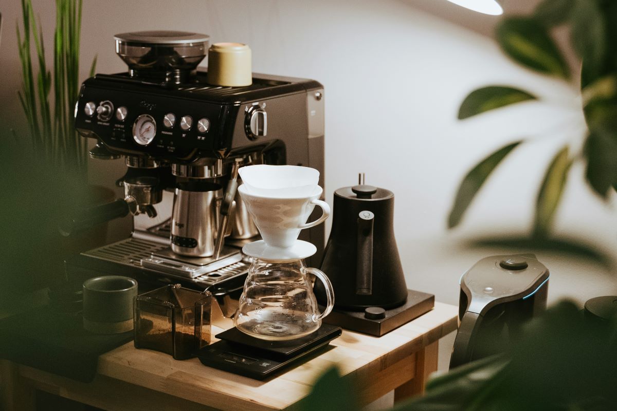 Compact home coffee station with a black espresso machine, white ceramic pour over cone above a glass carafe on a wooden counter