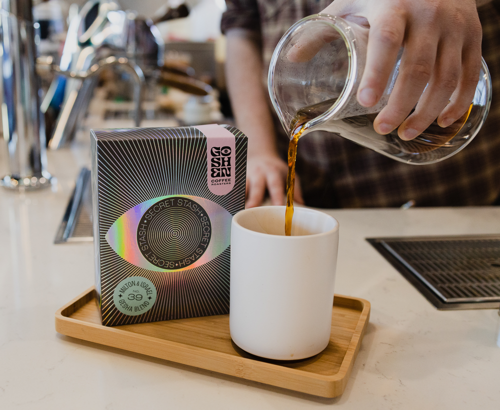 Pouring coffee into a white mug beside a Mistobox 2023 winner box on a wooden tray.