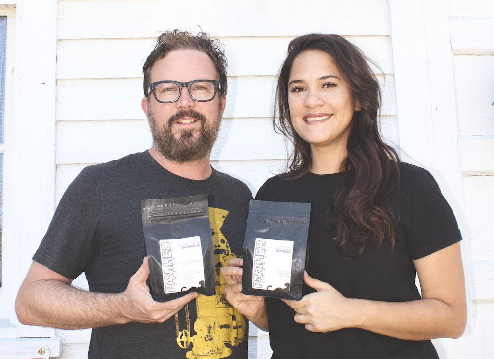 Two people outdoors posing with Panther Coffee Roasters coffee bags