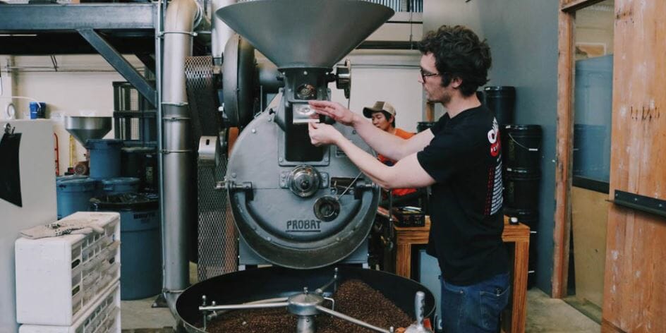 A barista adjusts a large Probat coffee roaster in a workshop.