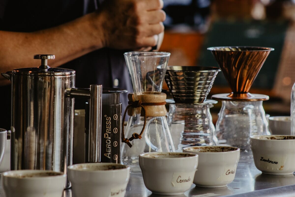 Coffee brewing station with Aeropress, kettle, glass carafes, and cups lined up on a counter