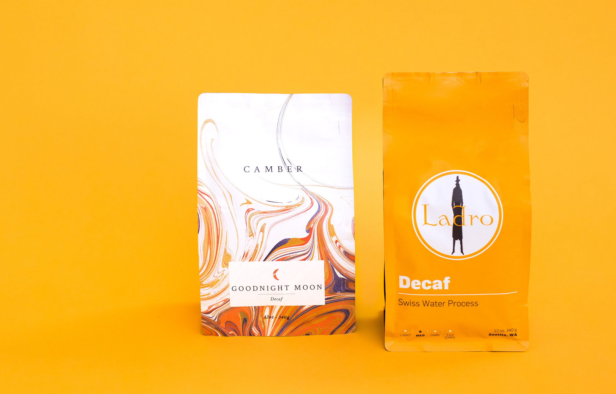 Two decaf coffee bags on an orange background, Camber marble design and Ladro Decaf packaging.