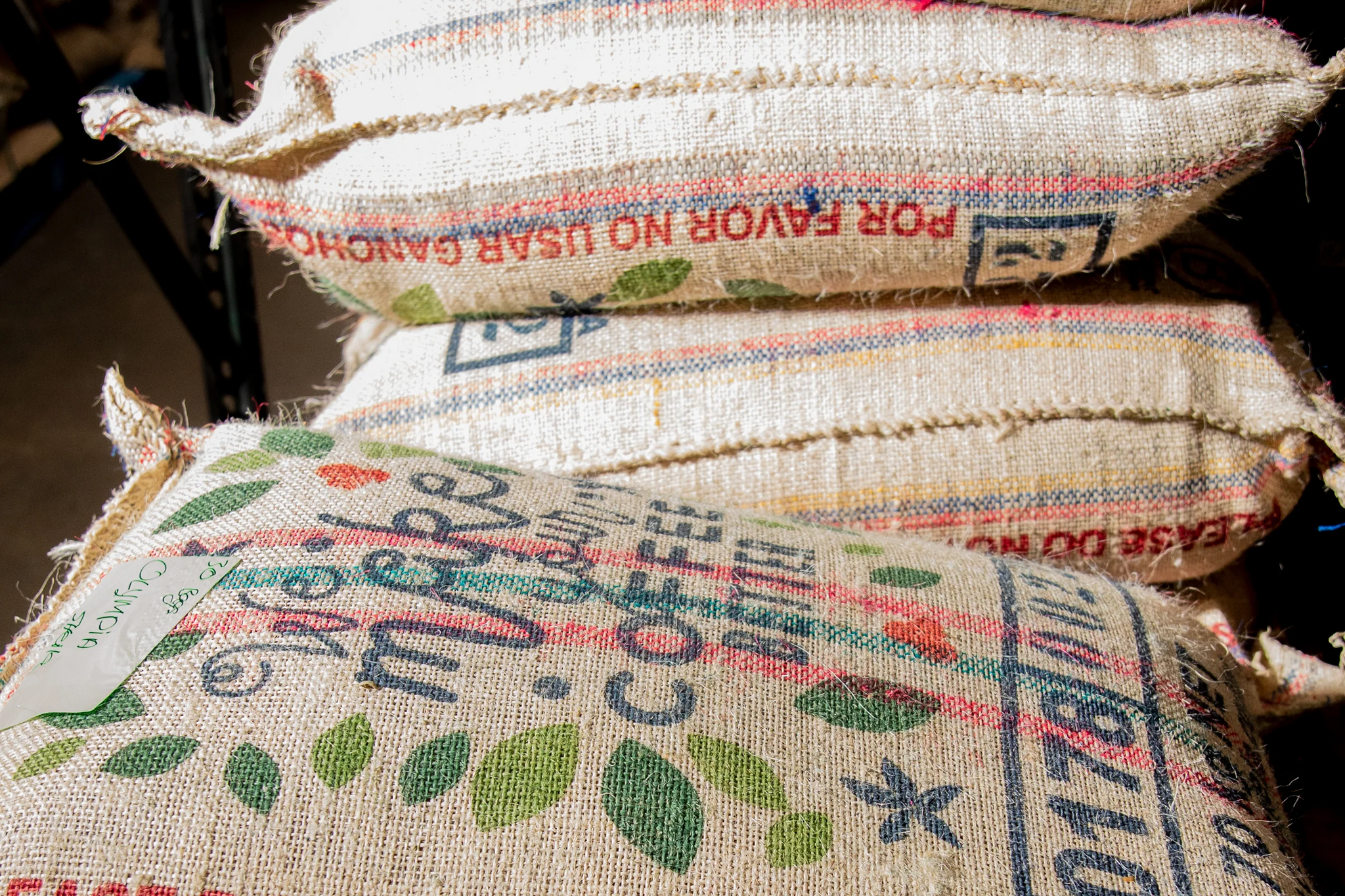 Stacked burlap coffee sacks with printed branding and colorful designs
